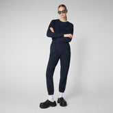 Fashion-forward model posing confidently in a monochromatic navy blue SaveTheDuck loungewear set, complemented by chunky black shoes and oversized sunglasses, embodying minimalist vegan fashion. | Save The Duck | Animal Free Elegant Duvets for Men and Women