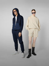 Man in navy blue hoodie and joggers with white sneakers, standing next to a woman in beige hoodie and shorts with black boots | Save The Duck | Animal Free Elegant Duvets for Men and Women