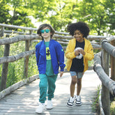 Two children walking on a wooden path wearing colorful eco-friendly jackets and sunglasses | Save The Duck | Animal Free Elegant Duvets for Men and Women