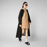 Woman modeling beige recycled polyester dress with black long coat and sandals | Save The Duck | Animal Free Elegant Duvets for Men and Women