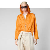 Woman wearing orange recycled polyester hooded jacket with beige pants and sunglasses | Save The Duck