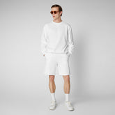Chic man in an all-white SaveTheDuck sweatshirt and shorts combo, paired with classic white sneakers and tinted sunglasses, showcasing sustainable casual wear. | Save The Duck | Animal Free Elegant Duvets for Men and Women