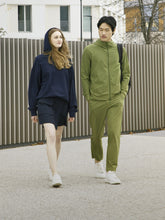 SaveTheDuck athleisure collection with a woman in a navy blue hoodie and skirt and a man in an olive green sporty tracksuit, showcasing animal-friendly athletic wear on an urban backdrop. | Save The Duck