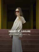 Smart Leisure by SaveTheDuck: Man in black athleisure with crossbody bag and woman in chic cream sweatshirt and pleated skirt, poised against a modern staircase with bold yellow accents. | Save The Duck