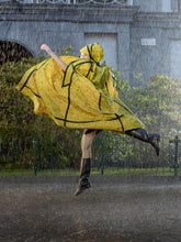 Energetic and lively, a woman twirls in the rain, her vibrant yellow animal-print cape swirling around her. The cape's bold black accents outline its dynamic flow, adding to the sense of motion. She sports a matching hood, sleek black leggings, and knee-high rain boots, perfect for the weather. Her leg kicked back in mid-twirl, she epitomizes the fusion of fashion and function, embracing the downpour with a spirit of joy. | Save The Duck